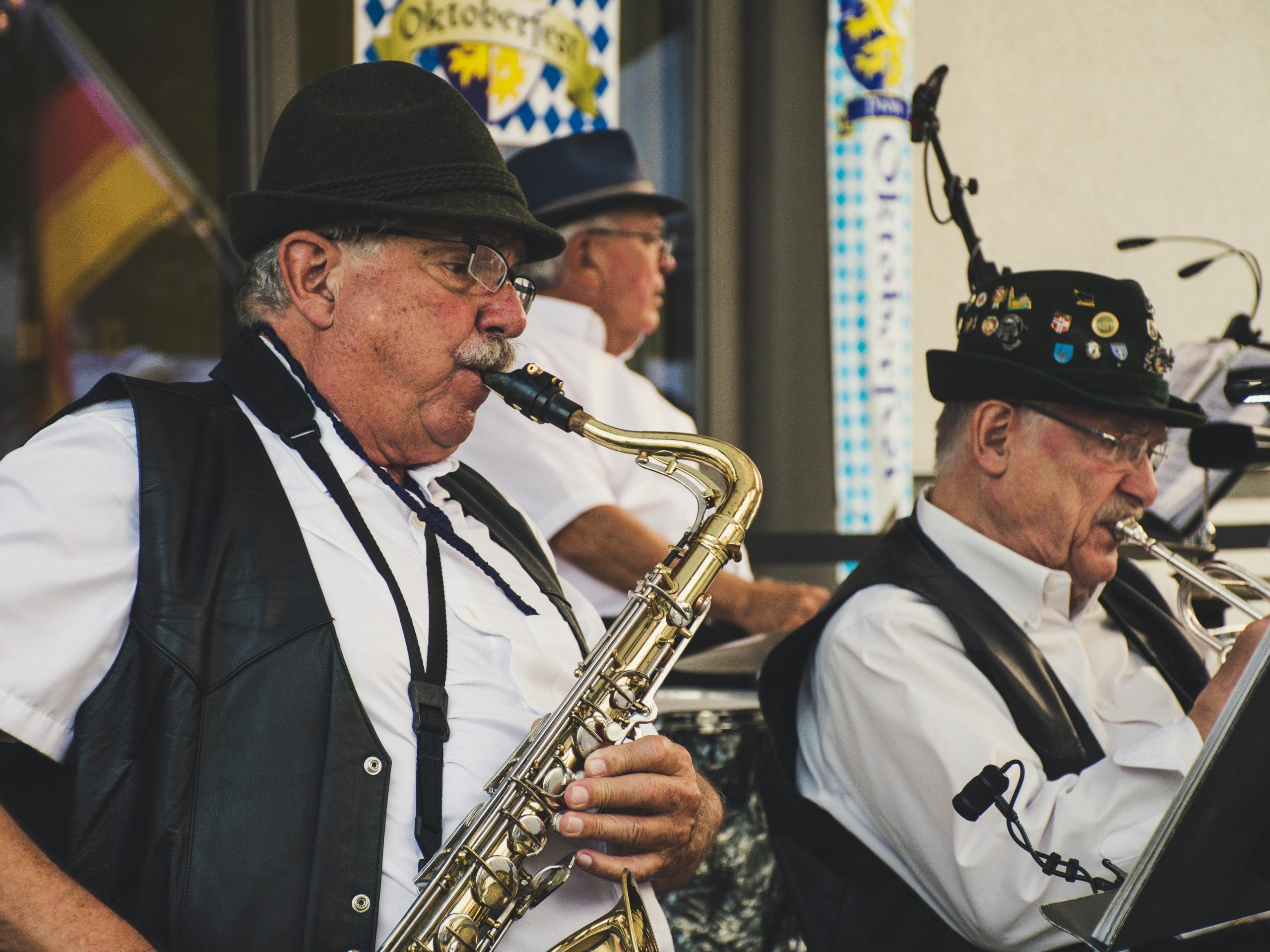Elderly musicians perform with saxophone and trumpet at an Oktoberfest festival outdoors.