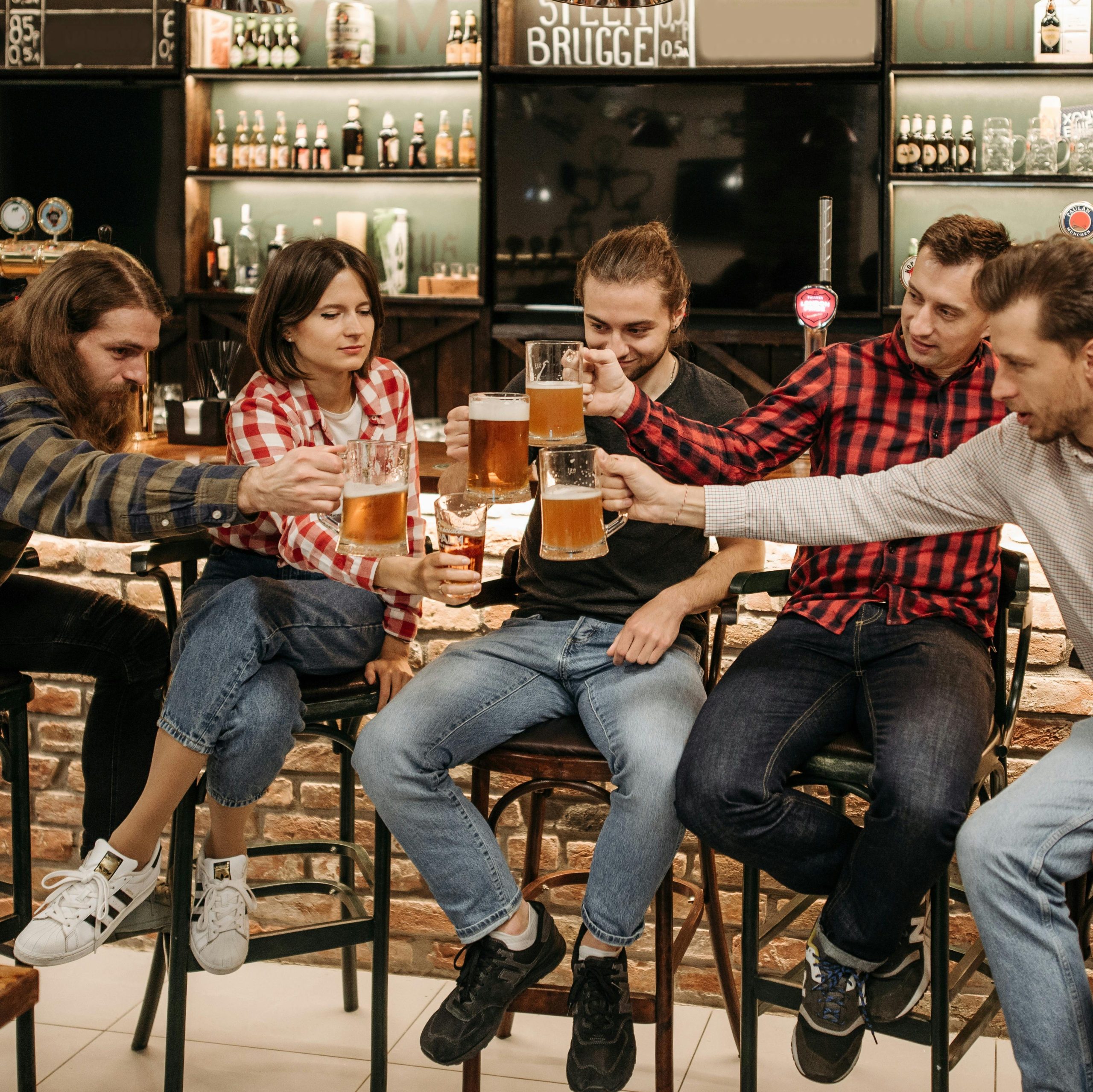 Five friends enjoying a toast with beer mugs at a cozy pub setting indoors.