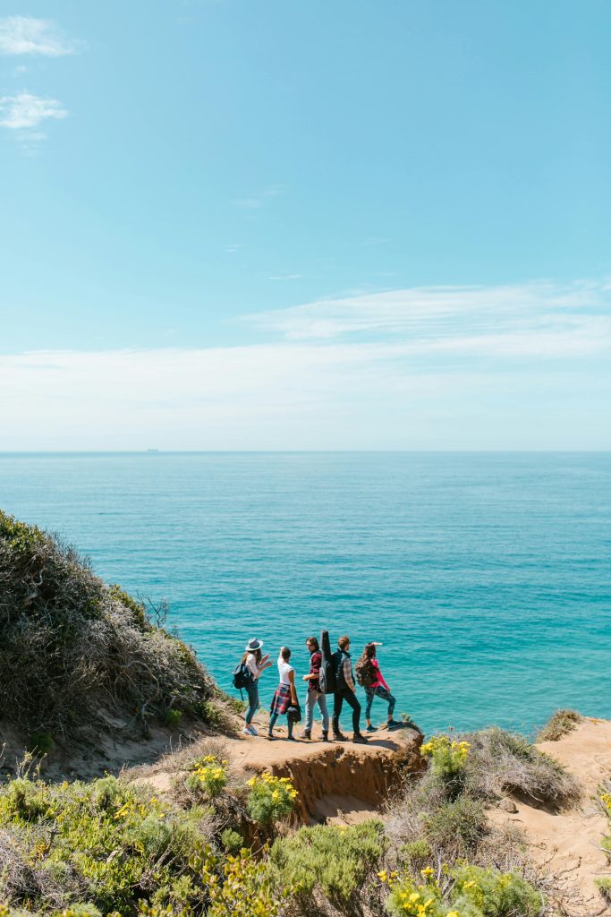 A group enjoys a scenic hike along a coastal cliff with ocean views and clear blue skies.