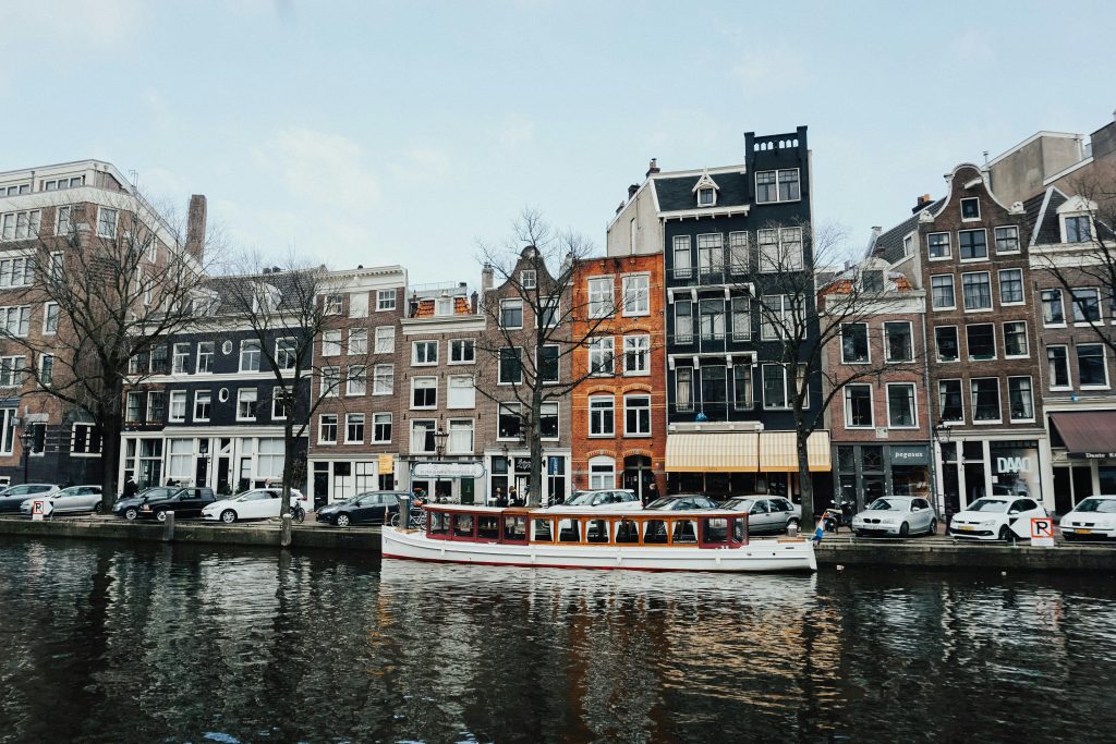 Charming Amsterdam canal scene with classic Dutch architecture and a boat cruising on the water.
