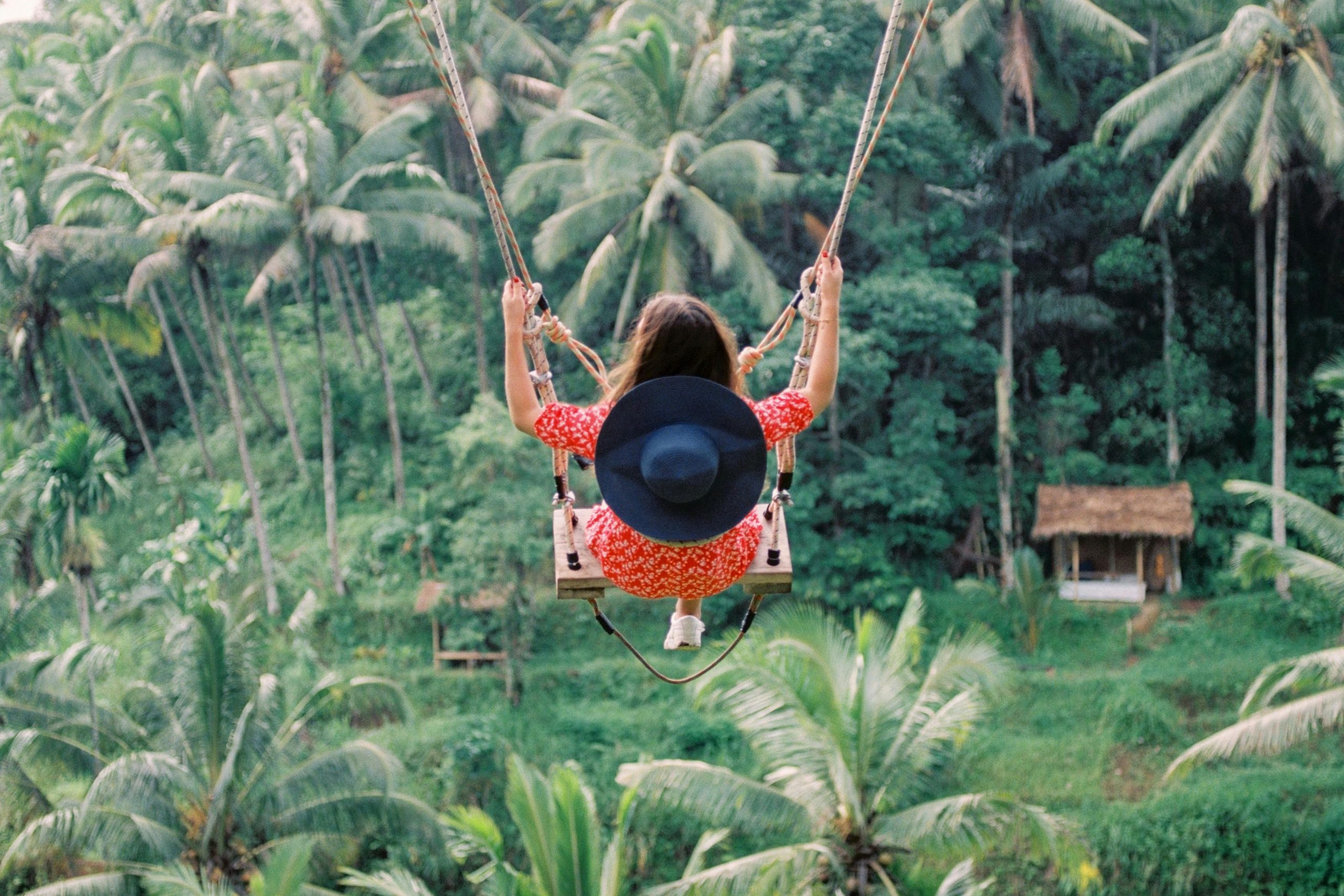 Woman enjoying a swing ride over lush tropical forest in Bali, Indonesia with palm trees surrounding.