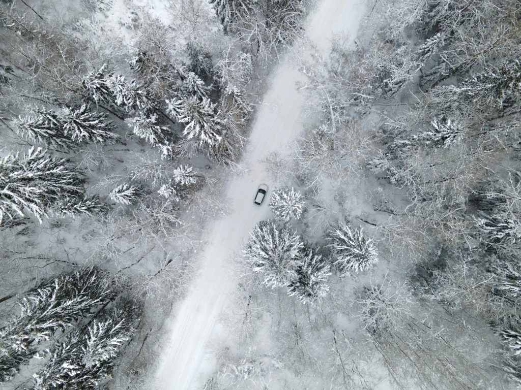 A car travels on a snowy road through a dense, snow-covered forest in winter.