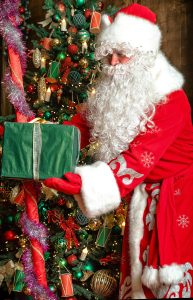 Santa Claus placing gifts by a decorated Christmas tree indoors.
