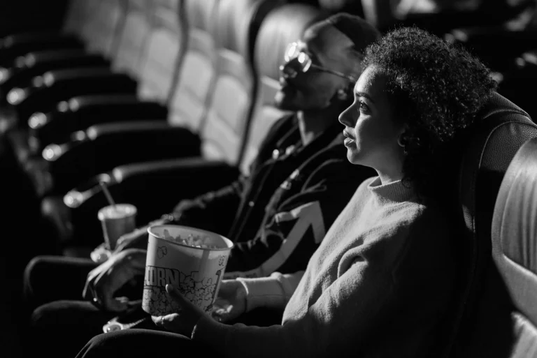 A couple sits together watching a movie in a classic black-and-white cinema setting.
